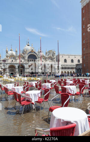 Acqua alta flooding in Piazza San Marco at midday  Venice, italy with water swirling arounf empty restaurant tables at midday in bright sunshine, Crow Stock Photo