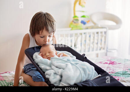 Beautiful boy, hugging with tenderness and care his newborn baby brother at home. Family love happiness concept