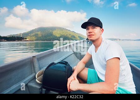 Side view of young man while traveling in boat on sea against tropical islands and blue sky. Stock Photo