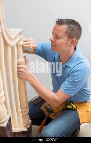 Carpenter Using Sandpaper On Bannister In Home Stock Photo