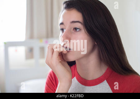Teenage Girl Sitting In Bedroom Biting Nails Stock Photo