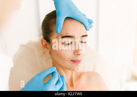 Skin check before plastic surgery. Beautician touch and draw correction lines on woman face. Stock Photo