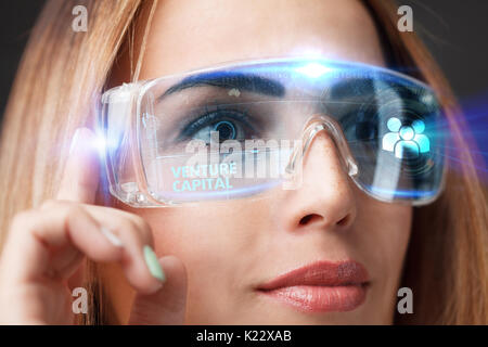 Young businesswoman working in virtual glasses, select the icon venture capital on the virtual display. Stock Photo