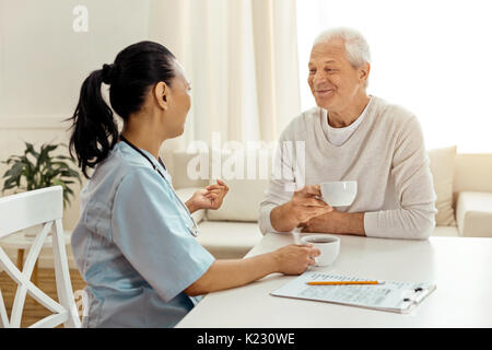 Positive nice caregiver and patient having tea Stock Photo