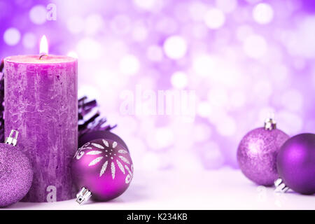 Purple and silver Christmas baubles and a candle in front of defocused purple and white lights. Stock Photo