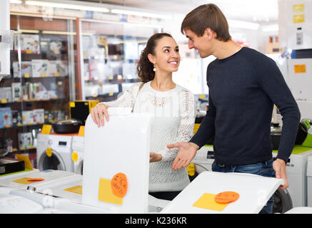 Young american couple choosing washing machine in hypermarket and smiling Stock Photo