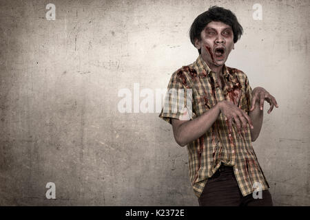 Spooky and bloody asian zombie man in a clothes standing against dirty background Stock Photo