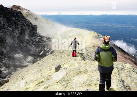 Mountain hiking on Kamchatka Peninsula: two young women tourists walking along sulfur fumarole field in summit crater of active Avacha Volcano. Stock Photo