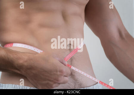 Always in good shape. Cropped image of muscular man measuring his waist  with measuring tape Stock Photo by gstockstudio