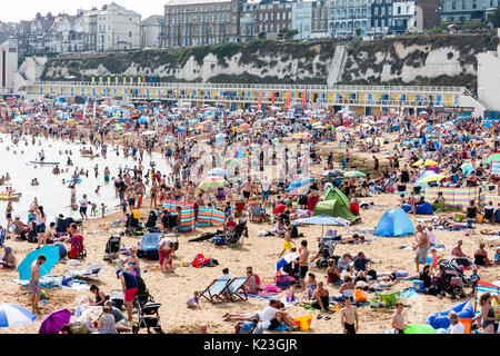 England, Viking Bay, Broadstairs. Beach totally packed with sun-seekers during period of hot weather. Beach and sea in view, masses of people on beach. Bright sunshine. Cliff and town in background. Stock Photo