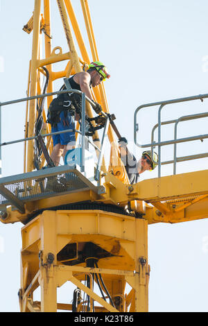 Workers in the process of removing a tower crane disassembling it bit by bit. The two main bolts holding the jib arm are loosened using a hammer. Stock Photo