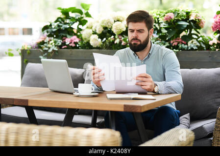 Frowning Businessman Reading Documents in Cafe Stock Photo
