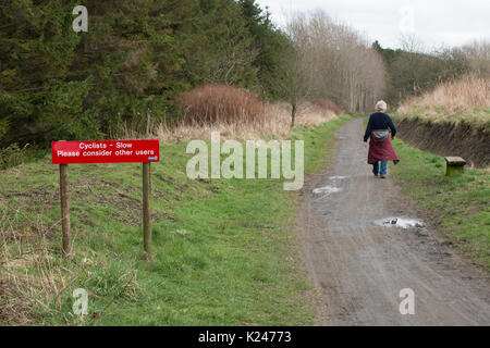 Public path in countryside showing lone walker and notice with request to cyclists to consider other path users Stock Photo