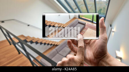 Two hands holding a mobile Smartphone and take a picture of a Modern living room with large windows and view on a automnal garden Stock Photo