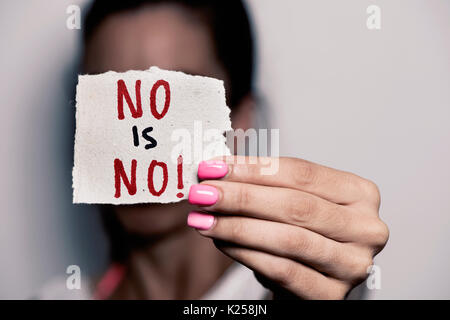 closeup of a young caucasian woman with pink polished nails holding a piece of paper with the text no is no written in it, in front of her face Stock Photo