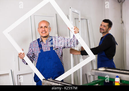Two positive professional workmen in coverall with different PVC windows and doors Stock Photo