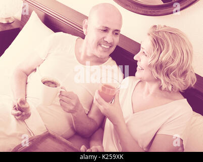 Happy smiling mature spouses having healthy breakfast in bed in the morning Stock Photo