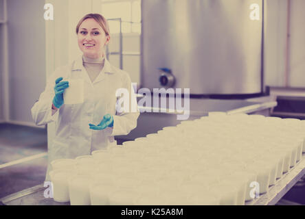 Portrait of woman dressed in white coat working on cottage cheese production on factory Stock Photo