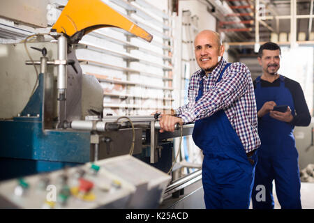 Two smiling workmen in overalls near cutter - lathe machine at factory Stock Photo