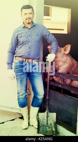 Mature farmer with a shovel standing next to a green tractor and ...