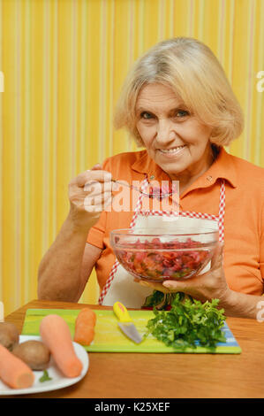 senior woman in white apron eating vegetable salad Stock Photo