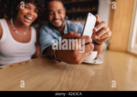 Young couple sitting together at cafe and taking selfie using mobile phone. Focus on hand of young man holding smart phone. Stock Photo