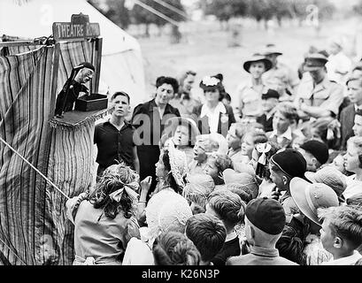 A wartime punch and Judy children's entertainment show - Location unknown but children's sun hats and Australian troops in background suggest Australia Stock Photo