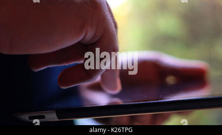 Closeup of man using tablet device in natural window light, shallow depth of field. Stock Photo