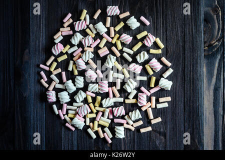Laid out in the shape of a circle multicolored marshmallows on black wooden table top view. Background of multi-colored and different in shape and siz Stock Photo
