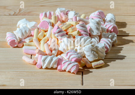 Multicolored marshmallows on bright wooden table. Background of multi-colored and different in shape and size of marshmallows. Sweets background Stock Photo