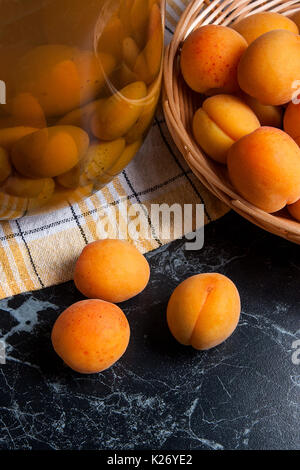 Ripe organic apricots harvested at summer time and big glass jar with canned sweet apricot compote on dark marble. Composition in rustic style - organ Stock Photo