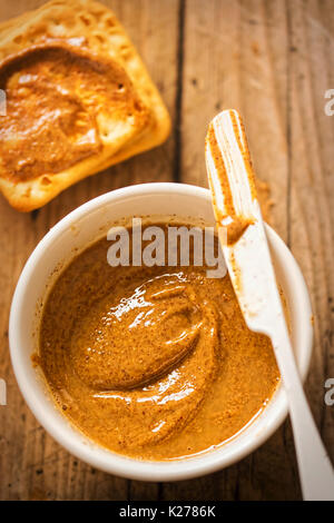 Almond butter in bowl with crackers on wooden table Stock Photo