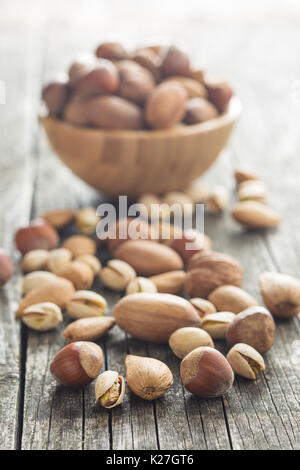 Different types of nuts in the nutshell. Hazelnuts, walnuts, almonds, pecan nuts and pistachio nuts on old wooden table. Stock Photo