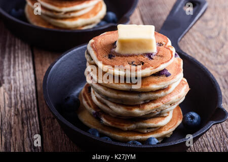 Pancakes with fresh blueberries topped with butter in cast iron skillet served for romantic brunch on rustic table Stock Photo