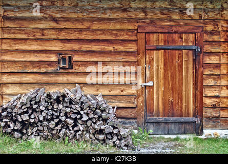 Log cabin wall with small window, door and small wood stack Stock Photo