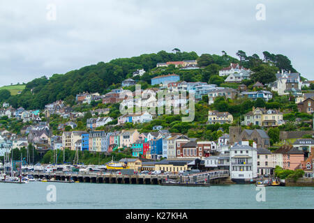 Coastal town of Dartmouth with colourful houses crammed on tree-cloaked hillside rising above harbour and ferry terminal in Devon, England Stock Photo