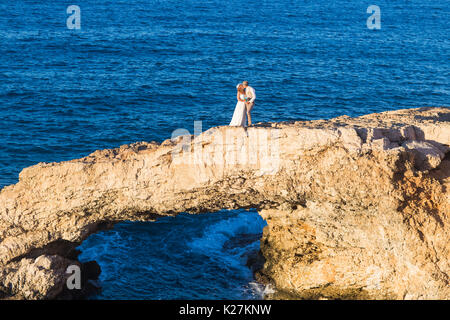 beautiful gorgeous blonde bride and stylish groom kissing on rocks, on the background of a sea, wedding ceremony on cyprus. Stock Photo