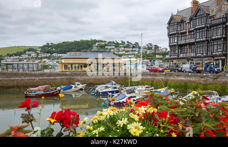 Panoramic view of English town of Dartmouth with elegant historic buildings bordering harbour, boats in calm water, & colourful flowers in foreground Stock Photo