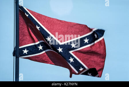 A flag currently flown to represent the now-defunct Confederate States of America is whipped by the wind on a flagpole in Tennessee, USA, one of the 13 states of the Confederacy represented by the 13 white five-pointed stars on two crossed blue bands trimmed with white against a red background. It is one of several flag designs used by Confederates fighting for the South during America's Civil War between 1861-1865. Stock Photo