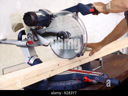 Closeup of hands of a person cutting wood lumber with a mitre saw, miter saw, circular blade. Stock Photo