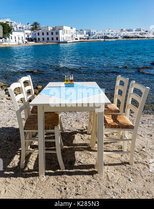 Vacant table and chairs set up on the beach waiting for diners to arrive, Mykonos, Greece. Stock Photo