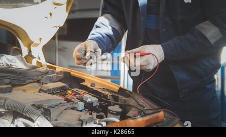 Mechanic in auto workshop works with car electrics - electrical wiring, voltmeter Stock Photo