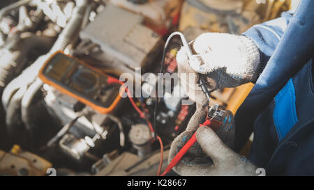Mechanic in auto workshop works with car electrics - electrical wiring, voltmeter - top view Stock Photo