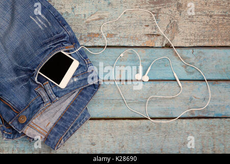 Touch smartphone-phone with headset-headset lined in the shape of a heart in a jeans pocket on a blue wooden background. Stock Photo