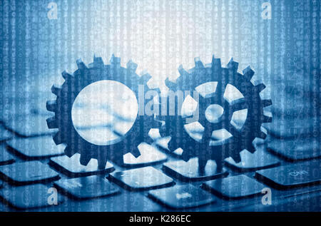 Two gears on computer keyboard with computer code in the background Stock Photo