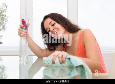 Happy long-haired girl cleaning glass  table with furniture polish at home Stock Photo