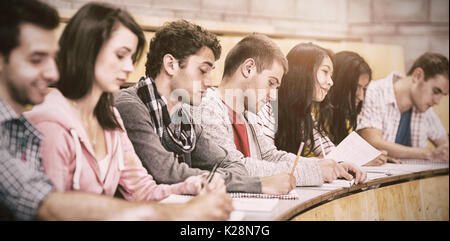 Students writing notes while sitting in row at lecture hall Stock Photo