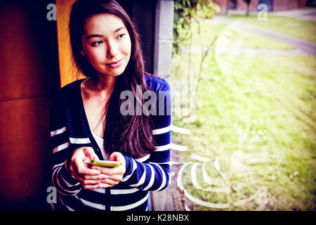 Smiling student with smartphone looking through window Stock Photo