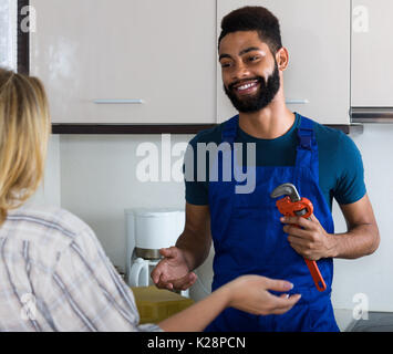 Young African plumber and happy white housewife in  kitchen Stock Photo