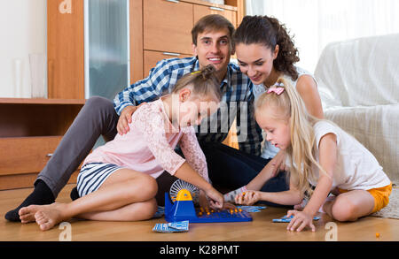 Smiling young parents with two little daughters playing at lotto at home Stock Photo